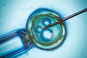 A close-up image of a needle injecting a cell, likely during in vitro fertilization, with blue and green coloring highlighting the cell and its internal structures.