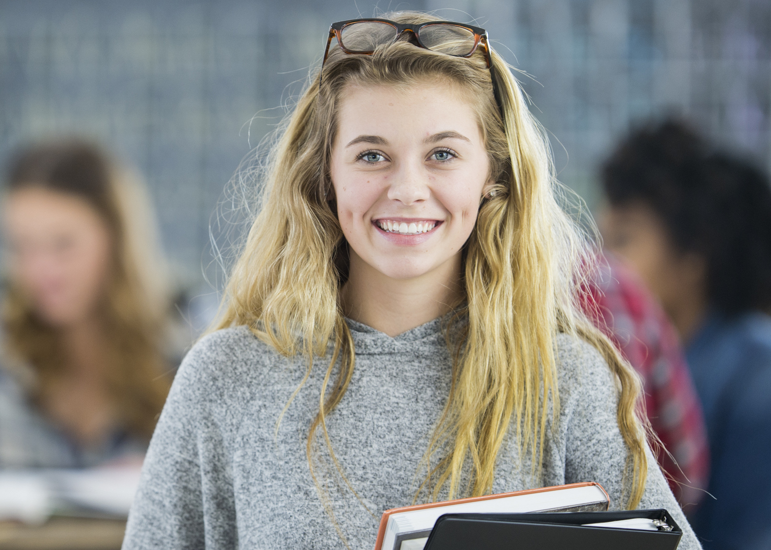A Caucasian woman is smiling and holding textbooks and binders