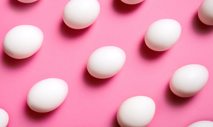 White eggs are arranged in a diagonal grid pattern on a bright pink background. The eggs are evenly spaced and their shadows create a sense of depth.