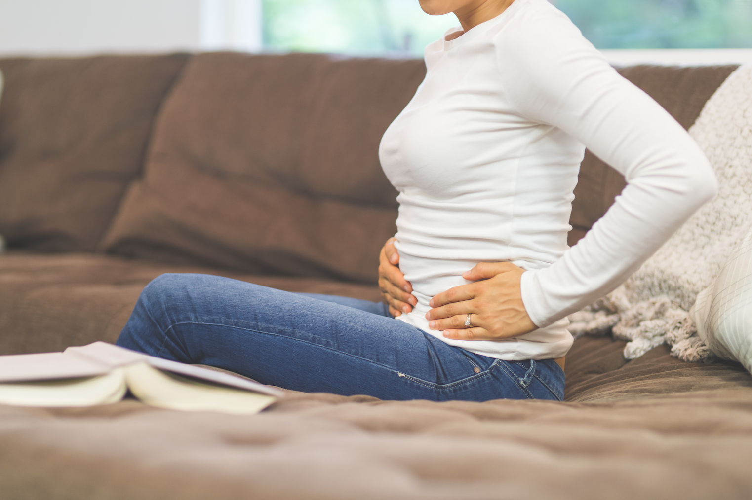 Woman sits on the couch and holds her pelvic area that is in pain