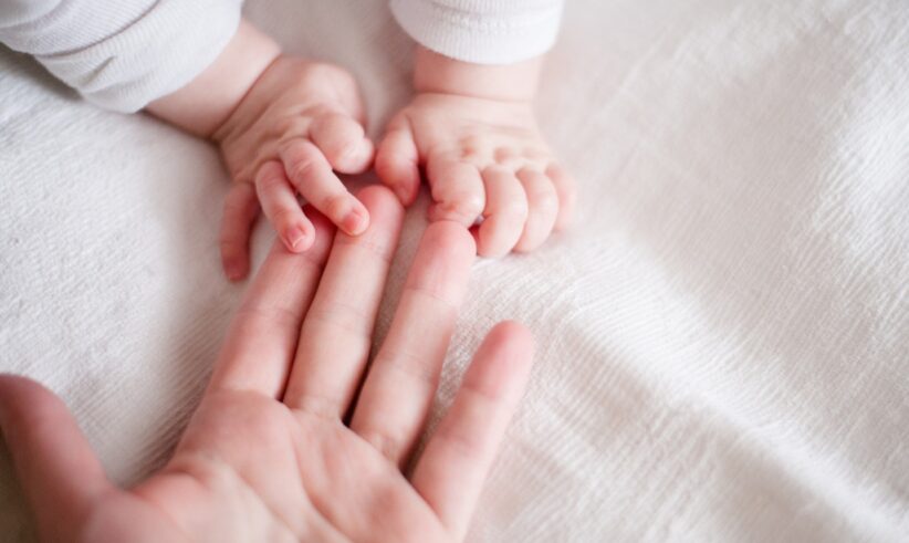 A babys hands gently grasp an adults finger on a soft white blanket. The adults hand is open, and the babys small hands rest on top, creating a tender, intimate moment.
