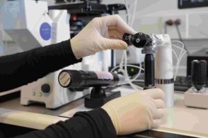 A person wearing gloves adjusts scientific equipment in a laboratory setting, surrounded by various instruments and cables on a workbench.