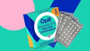 A box of Opill Daily Oral Contraceptive is shown next to three blister packs of pills, set against a colorful pink, blue, and green background.