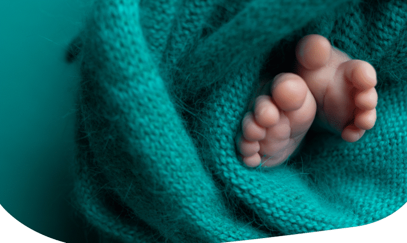 Close-up of a newborn babys feet wrapped in a soft, teal knitted blanket, with the tiny toes peeking out.