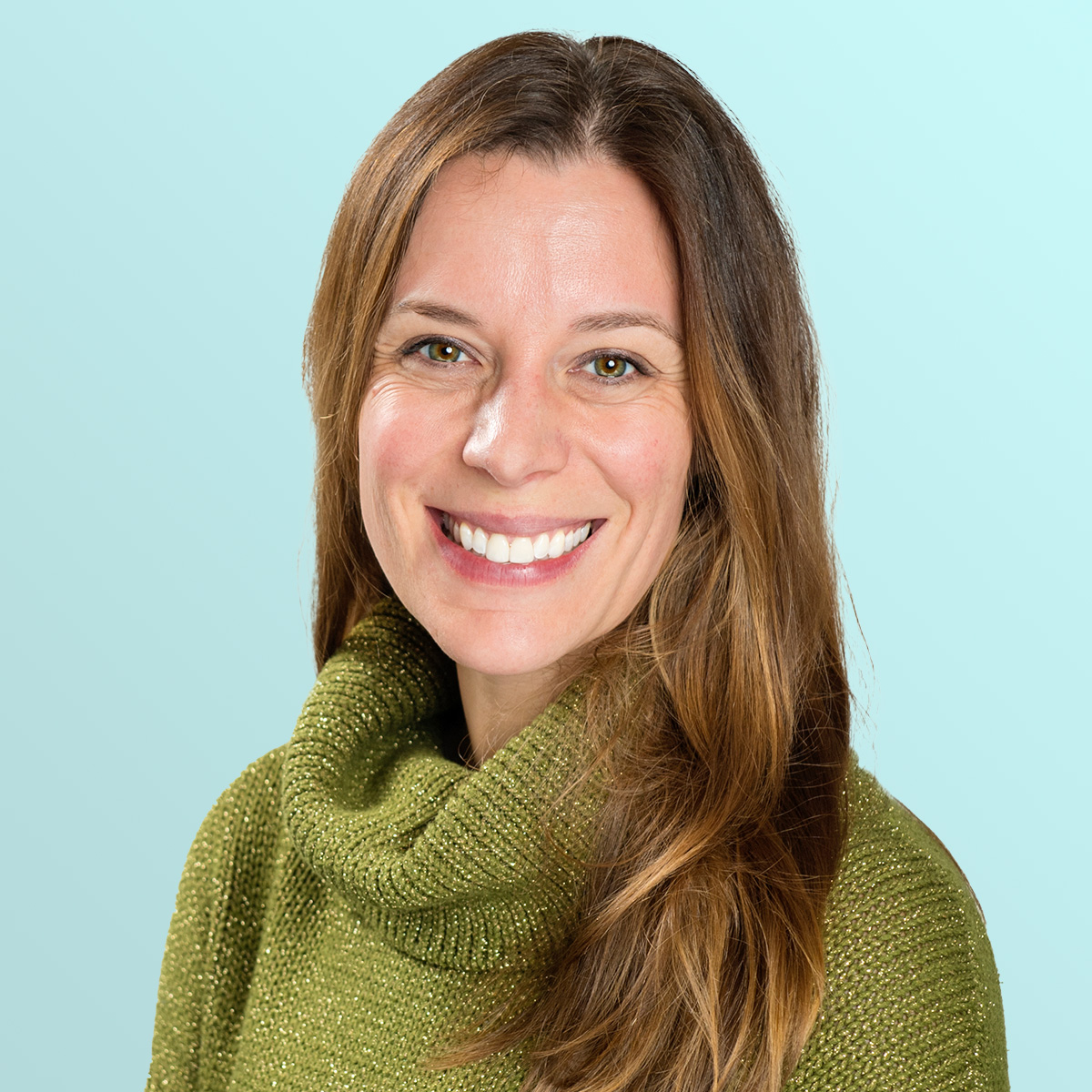 A woman with long brown hair, wearing a green turtleneck sweater, smiling against a light blue background.