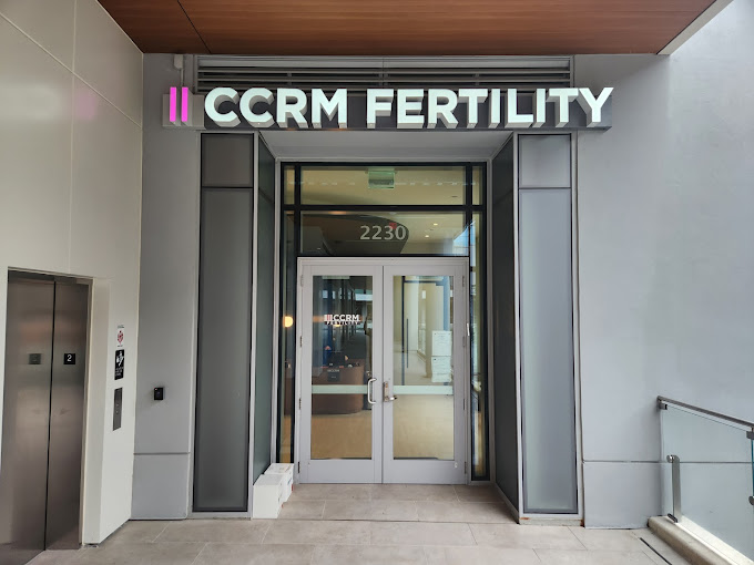 The entrance to CCRM Fertility, with glass double doors under a sign that says CCRM Fertility in bright white letters. The building number 2230 is displayed above the doors.