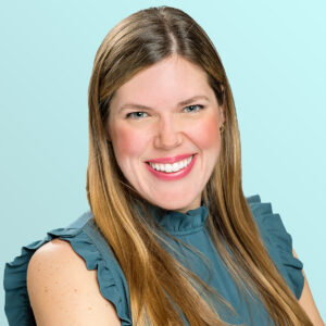 A woman with long, straight light brown hair smiles at the camera. She is wearing a ruffled, sleeveless teal blouse and is posed against a light blue background.