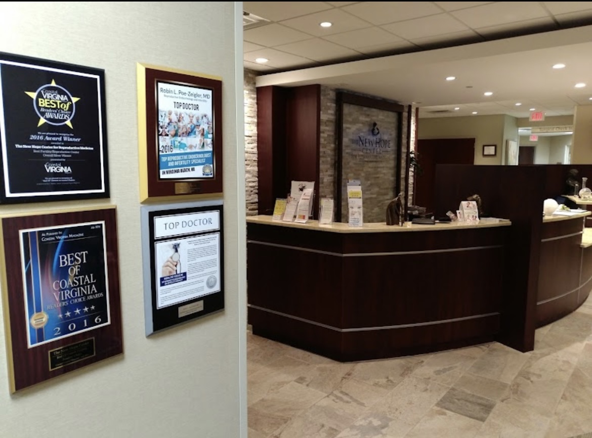A modern medical office reception area with a curved desk, brochures, and awards displayed on the wall. The space has tiled floors, warm lighting, and a welcoming atmosphere.