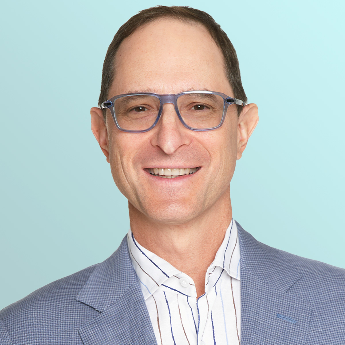A smiling man wearing clear glasses, a light blue checkered blazer, and a white shirt with blue stripes, posed in front of a light blue gradient background.