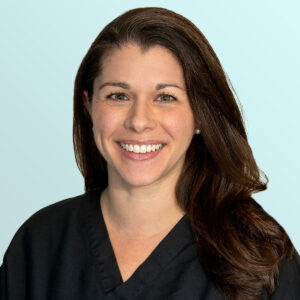A woman with long brown hair wearing a black V-neck top smiles at the camera against a light blue background.