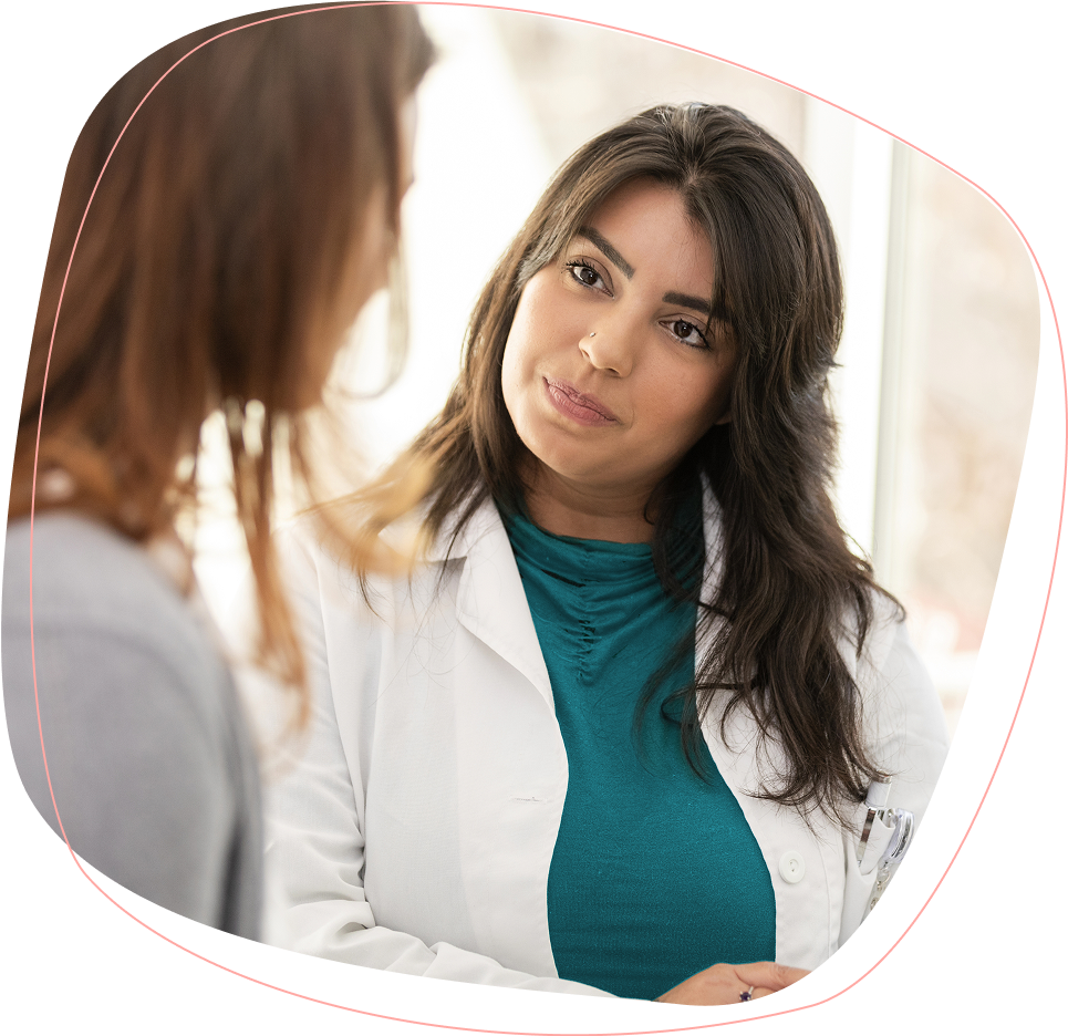 A female doctor in a white coat listens attentively to a patient during a consultation in a bright, modern office setting.