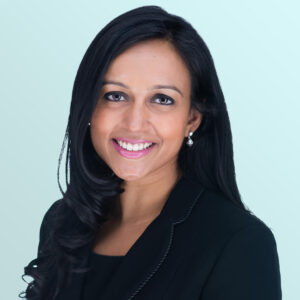 A woman with long, dark hair wearing a black blazer and a black top smiles at the camera against a light blue background.