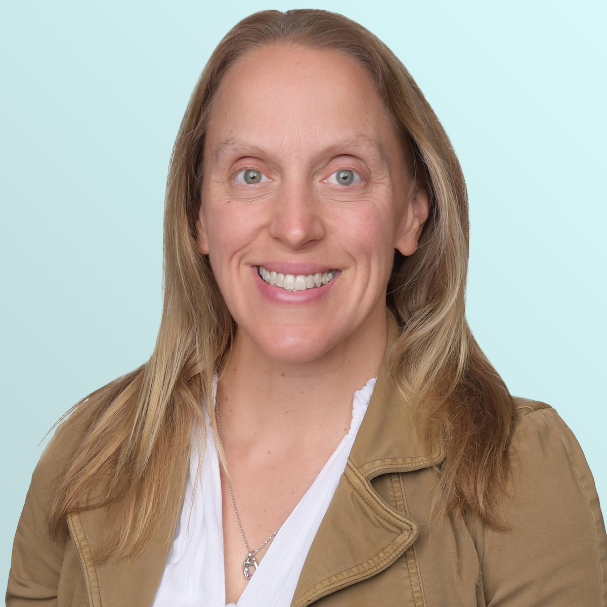 A woman with long light brown hair, wearing a tan jacket over a white blouse, smiles at the camera against a light blue background.