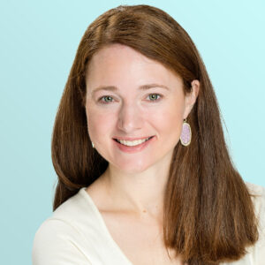 A woman with long brown hair wearing a white top and oval-shaped earrings smiles at the camera in front of a light blue background.