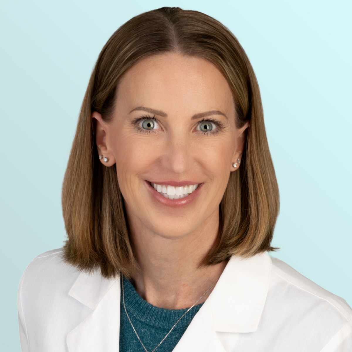 A woman with straight, shoulder-length light brown hair smiles at the camera. She is wearing a white lab coat over a teal top, with stud earrings and layered necklaces. The background is a light blue gradient.