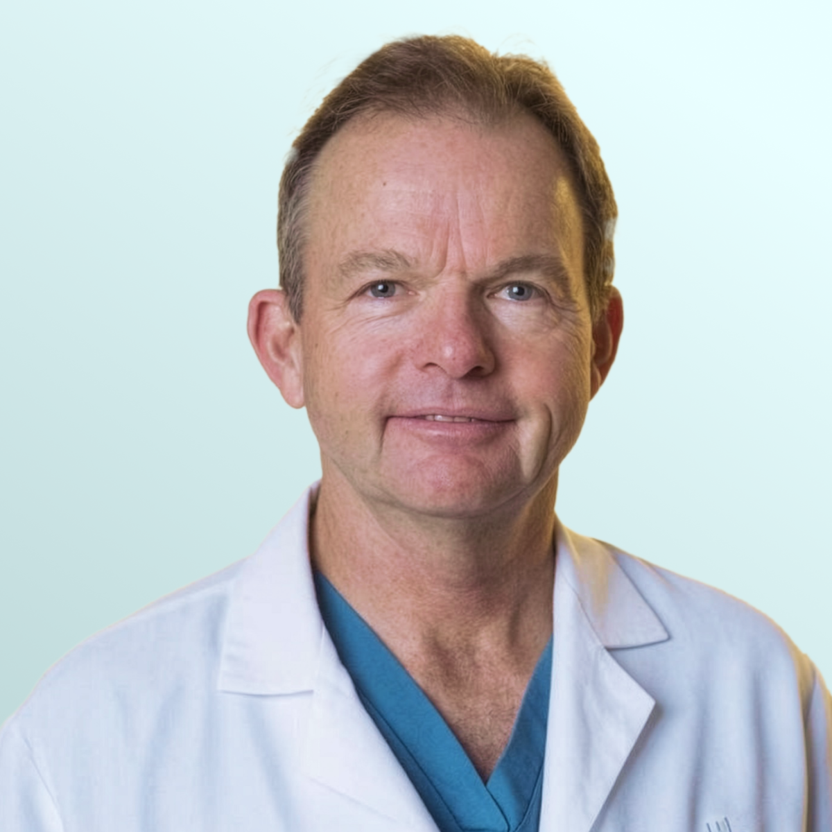 A middle-aged man with short brown hair, wearing a black suit, white shirt, and blue patterned tie, poses against a light blue gradient background.
