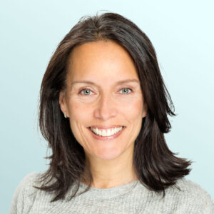 Smiling woman with straight, dark brown hair wearing a light grey sweater, posed against a light blue background.