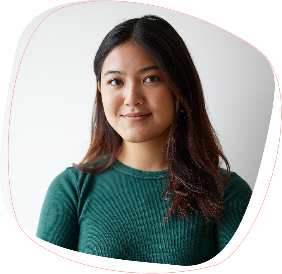A young woman with long dark hair, wearing a green ribbed sweater, stands against a plain white background, smiling softly at the camera.