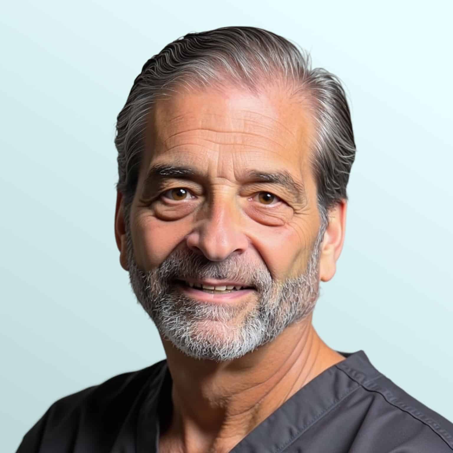 A mature man with gray hair and beard, wearing a navy suit, white shirt, and patterned tie, poses against a light blue background.