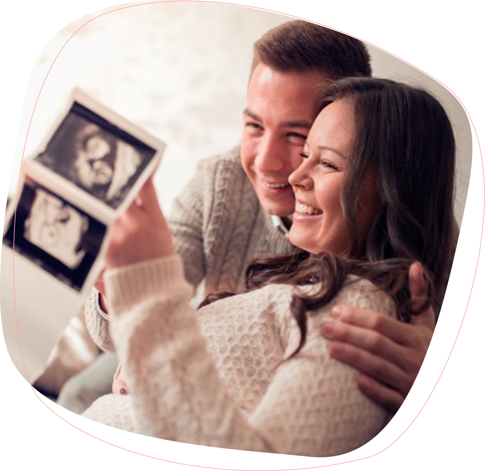 A smiling couple sits close together, holding and looking at ultrasound images, appearing happy and excited about their pregnancy.