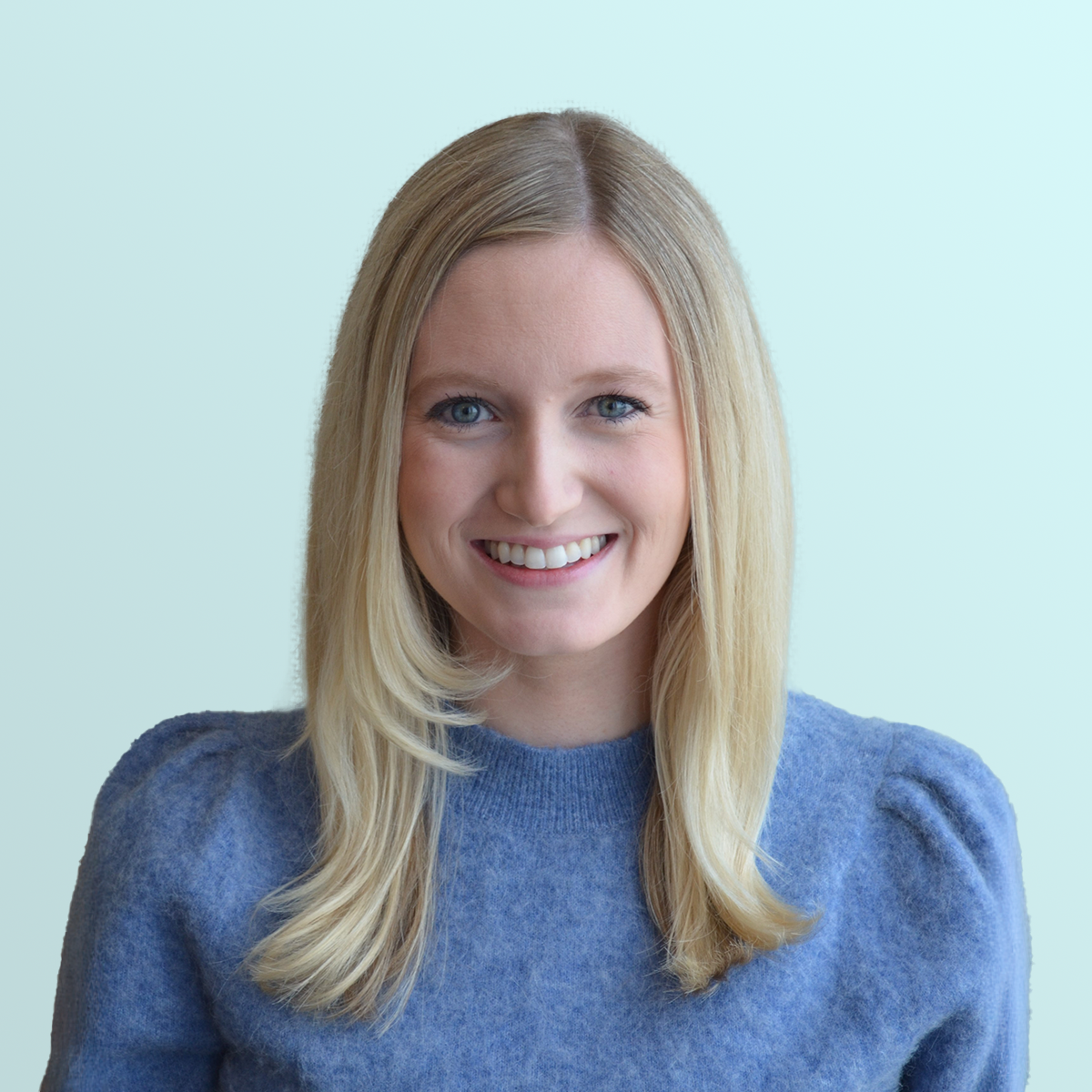 A woman with straight blonde hair and blue eyes is smiling at the camera. She is wearing a soft blue sweater and is posed against a light blue background.