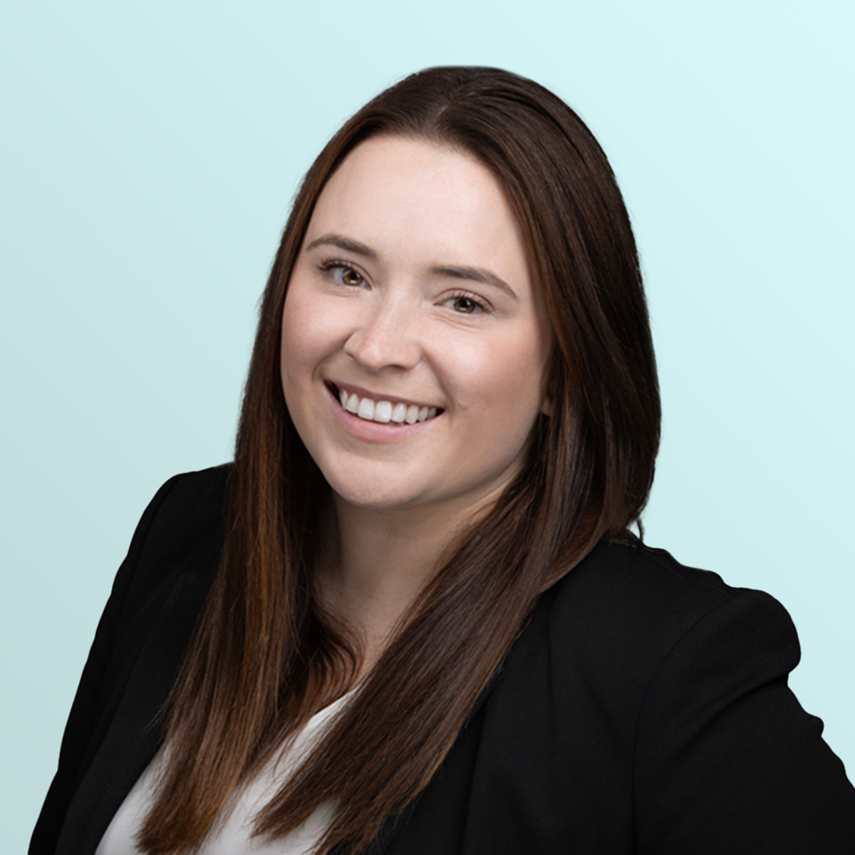 A woman with long straight brown hair, wearing a black blazer and white top, smiles at the camera against a light blue background.