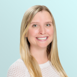 A smiling young woman with long straight blonde hair, wearing a white textured sweater, poses in front of a light blue background.