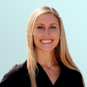 A woman with long, straight blonde hair and blue eyes smiles at the camera. She is wearing a black top and is posed against a plain, light blue background.