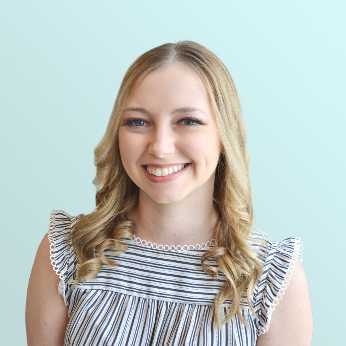 A young woman with long blonde hair and blue eyes smiles at the camera. She is wearing a black and white striped top with ruffled sleeves, and the background is a solid light blue color.