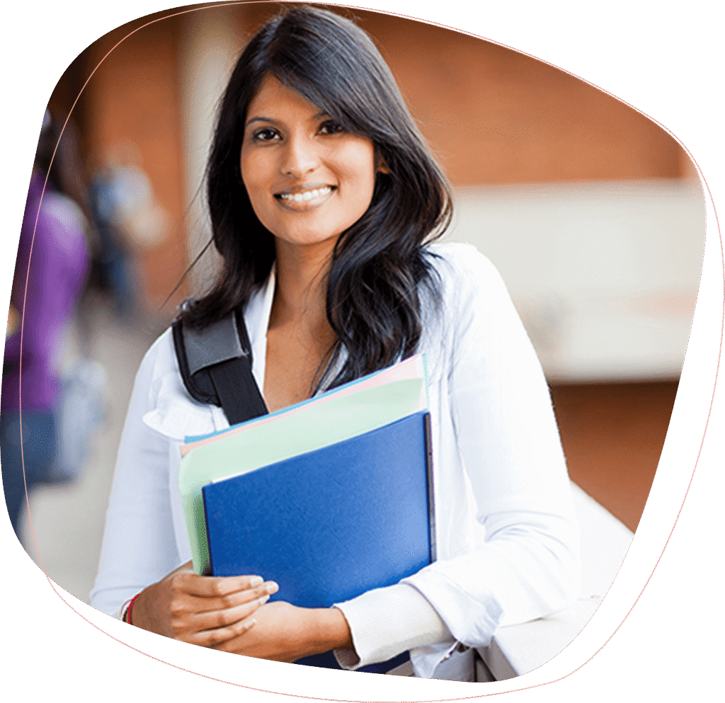 A young woman with long dark hair, wearing a white blouse and carrying a backpack, holds folders and smiles while standing outdoors near a brick building.