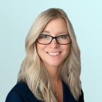 A woman with long, wavy blonde hair and glasses smiles at the camera. She is wearing a dark blazer and a necklace, with a light blue background.