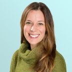 A woman with long brown hair, wearing a green turtleneck sweater, smiling against a light blue background.