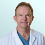 A middle-aged man with short brown hair, wearing a black suit, white shirt, and blue patterned tie, poses against a light blue gradient background.