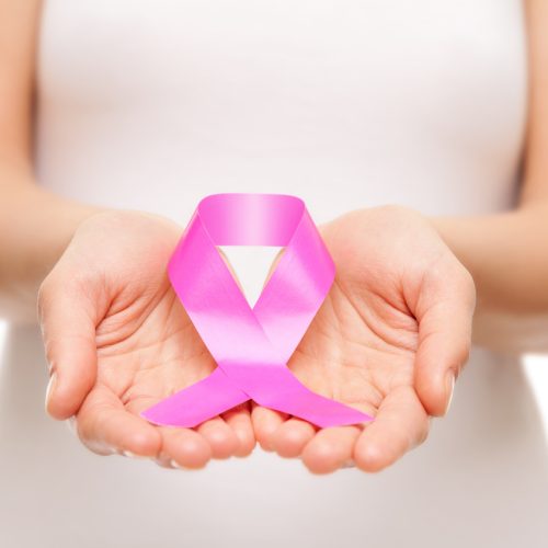 A person in a white shirt holds a pink ribbon in their cupped hands, symbolizing breast cancer awareness.