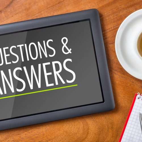 A tablet displaying the words Questions & Answers sits on a wooden table next to a cup of espresso and a notepad with a pen.