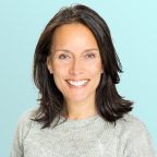 Smiling woman with straight, dark brown hair wearing a light grey sweater, posed against a light blue background.