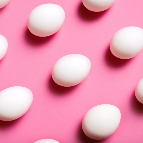 White eggs are arranged in a diagonal grid pattern on a bright pink background. The eggs are evenly spaced and their shadows create a sense of depth.