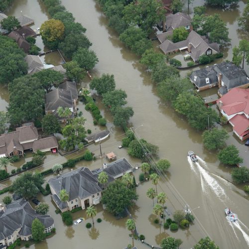Aerial view of a flooded residential neighborhood with streets submerged, houses surrounded by water, and two boats navigating through the flooded area.