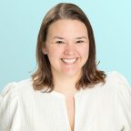A woman with shoulder-length brown hair smiles at the camera. She is wearing a textured white top and is posed in front of a light blue background.