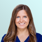 A woman with long brown hair and blue eyes, wearing a navy blue top, smiling at the camera against a light blue background.