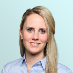A woman with long blonde hair, wearing a light blue collared shirt, smiles slightly in front of a light blue background.
