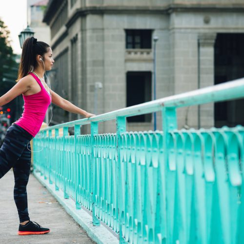 Sporty Asian woman stretching legs after jogging in the city