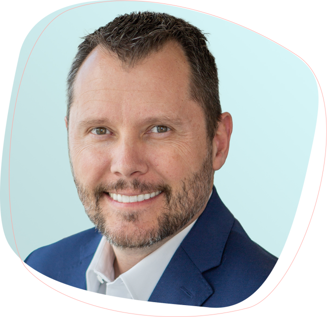 Wade_Lowder-Desktop Smiling man with short dark hair and beard wearing a navy blue suit jacket and white shirt, posed against a light blue background.
