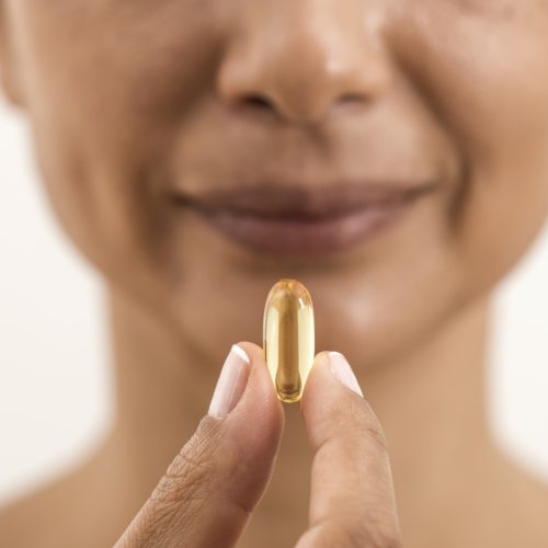 A person holds a yellow translucent capsule between their fingers, close to their mouth, with a slight smile visible on their face.