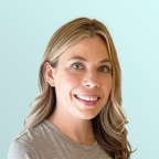 A woman with long, light brown hair and hazel eyes smiles at the camera. She is wearing a grey top and small earrings, with a light blue background behind her.