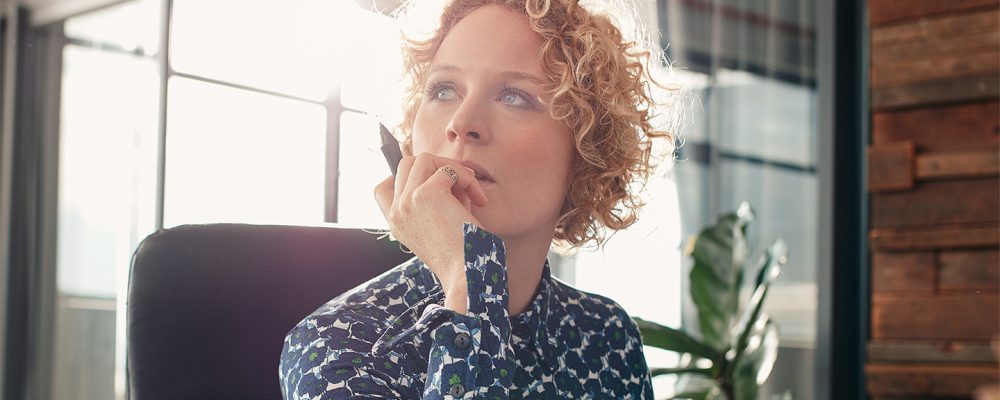 Portrait of young female designer sitting at her desk looking away and thinking.