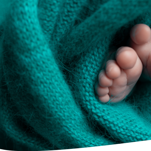 Close-up of a newborn babys feet wrapped in a soft, teal knitted blanket, with the tiny toes peeking out.